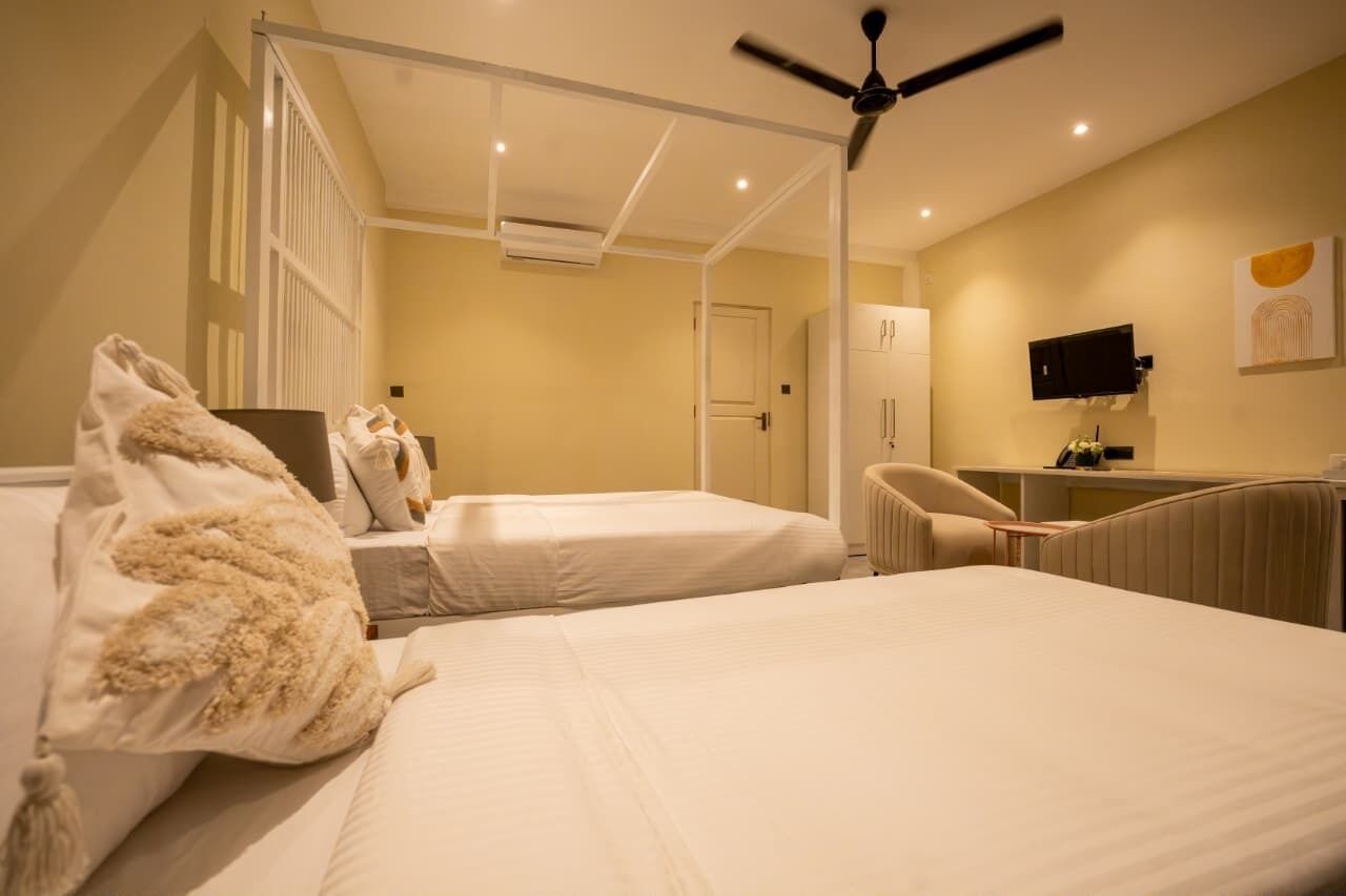 Une chambre d’hôtel avec deux lits, un ventilateur de plafond, une télévision et un bureau.