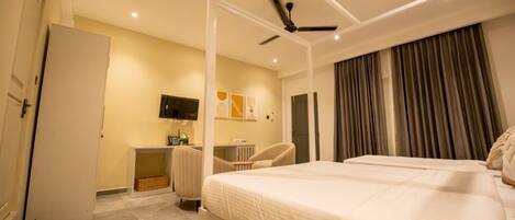 A modern hotel room with a large bed, a desk, a chair, a television, and a ceiling fan.