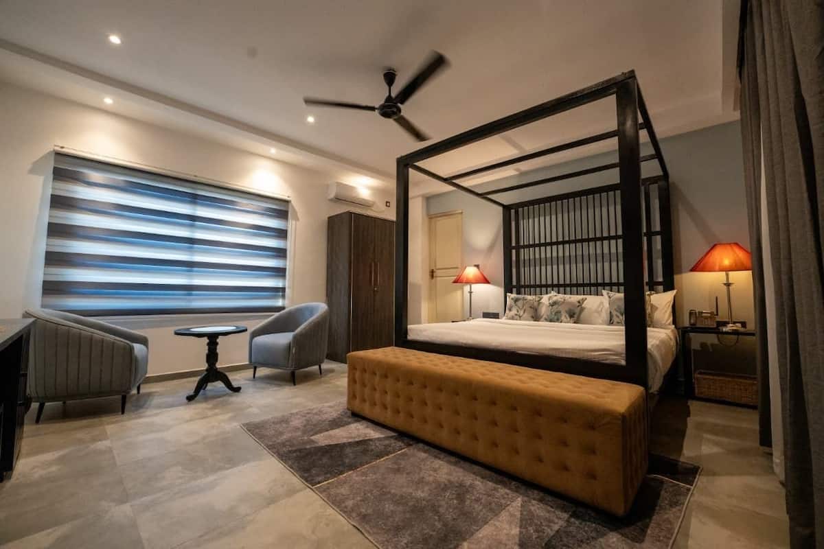 A modern bedroom with a four-poster bed, a sitting area with a bench, a desk, and two lamps.