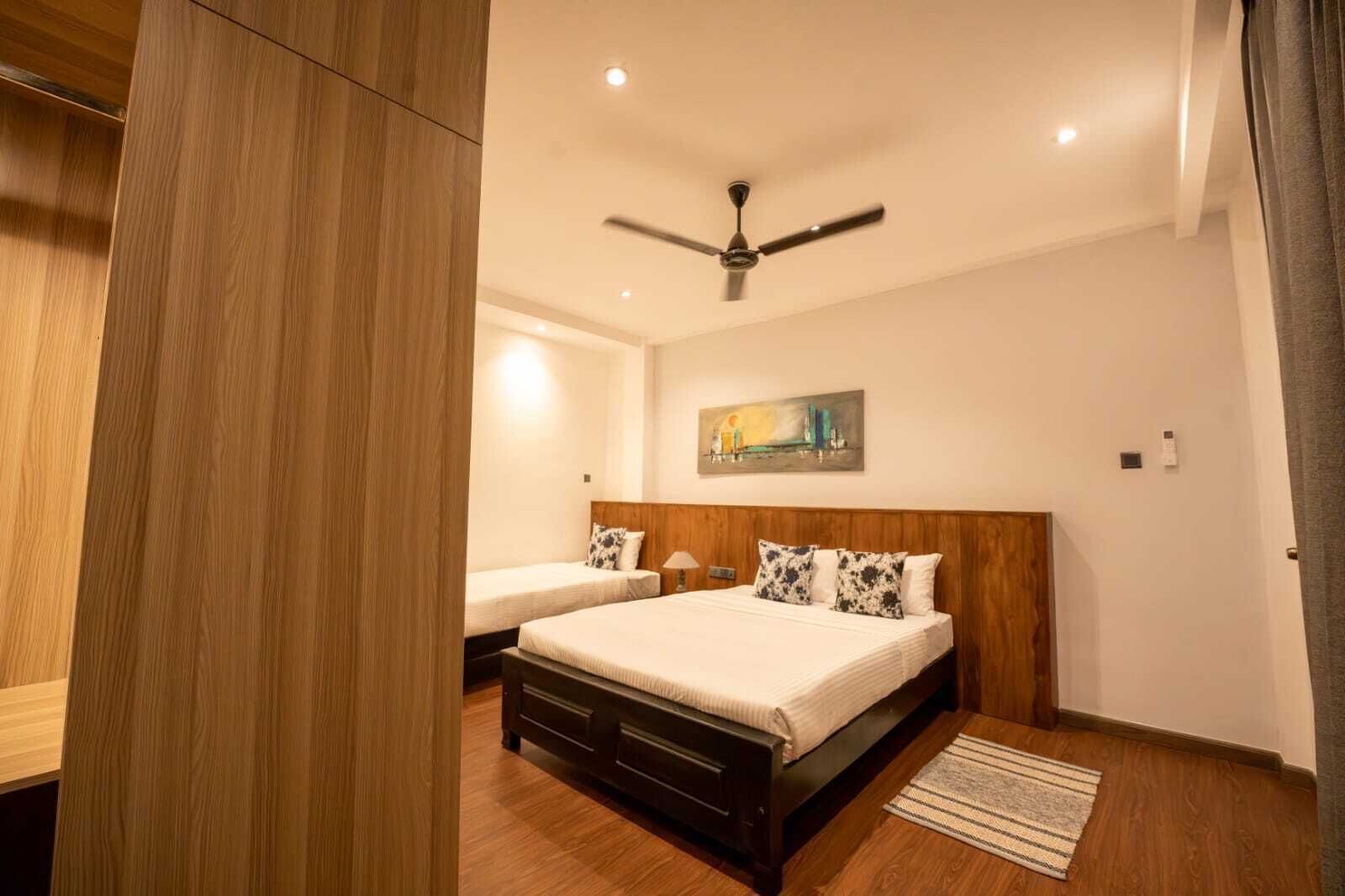 A bedroom with two beds, a ceiling fan, a painting, and a wooden floor.