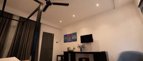 A modern hotel room with a bed, a desk, a chair, a TV, and a ceiling fan.
