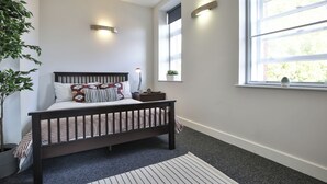 Un dormitorio con una cama de madera oscura, una mesita de noche con una lámpara, una ventana que ofrece vistas a zonas verdes y una planta en maceta.
