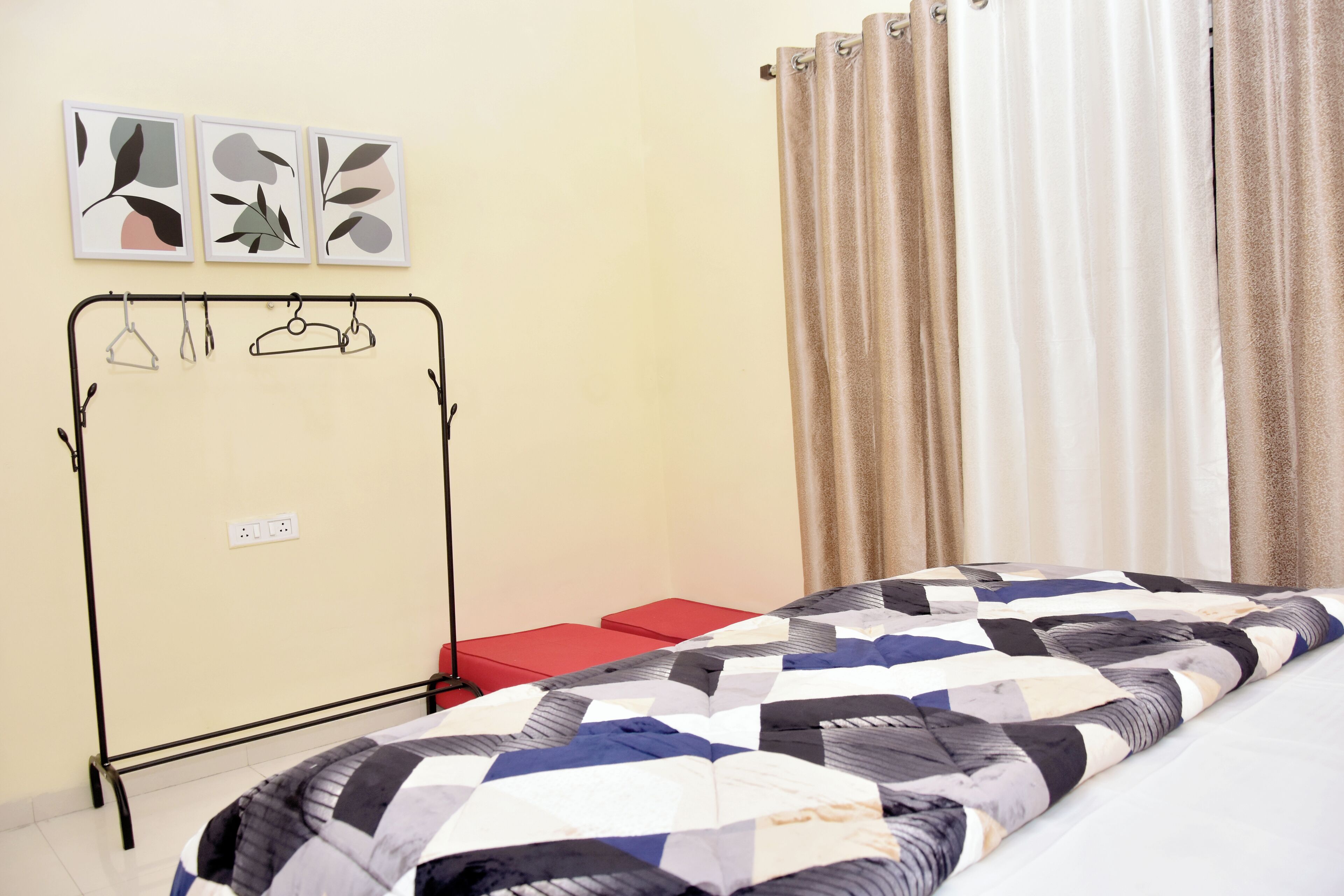 A bedroom with a bed, a red bench, a metal wardrobe, and three framed pictures on the wall.