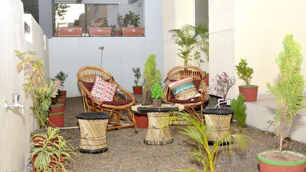 Un patio con mobiliario de mimbre, incluyendo dos sillas y una mesita, rodeado de macetas con plantas.