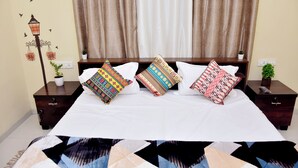 Una cama bien hecha con almohadas estampadas, una lámpara decorativa de pared y una pequeña planta en una mesita de noche.