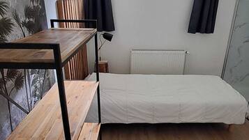 A small, single-room accommodation with a wooden floor, a simple bed, a table, and a chair.