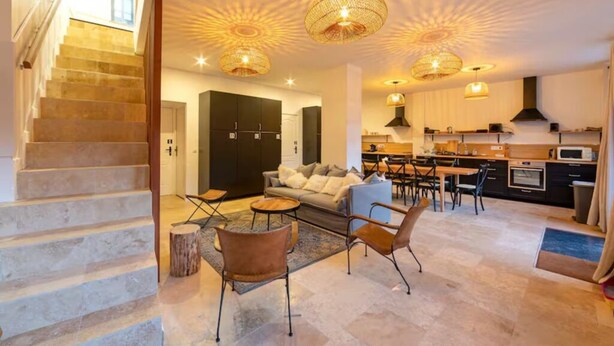 Uma sala ampla com escada, sofá, mesa de centro e área de jantar com cadeiras e mesa.