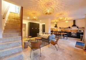 A spacious living area with a staircase, a sofa, a coffee table, and a dining area with chairs and a table. - Sophie's House (Rencurel)