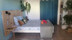 Ein Bett mit Holz Kopfteil, ein Nachttisch und ein Beistelltisch. Auf jeder Seite des Bettes stehen je eine Zimmerpflanze in Töpfen.