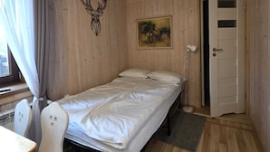 Pieni, viihtyisä huone, jossa on puinen katto ja seinät, yksi sänky, työpöytä tuolilla ja ovi.