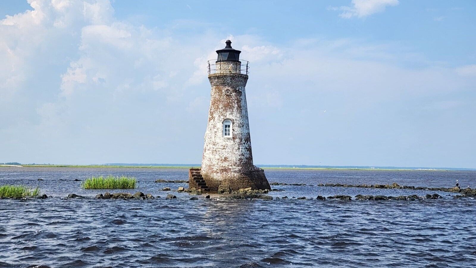 Un faro junto a un cuerpo de agua tranquilo bajo un cielo despejado.