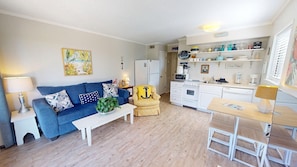 A compact living space with a sofa, coffee table, armchair, kitchenette, and a dining area.