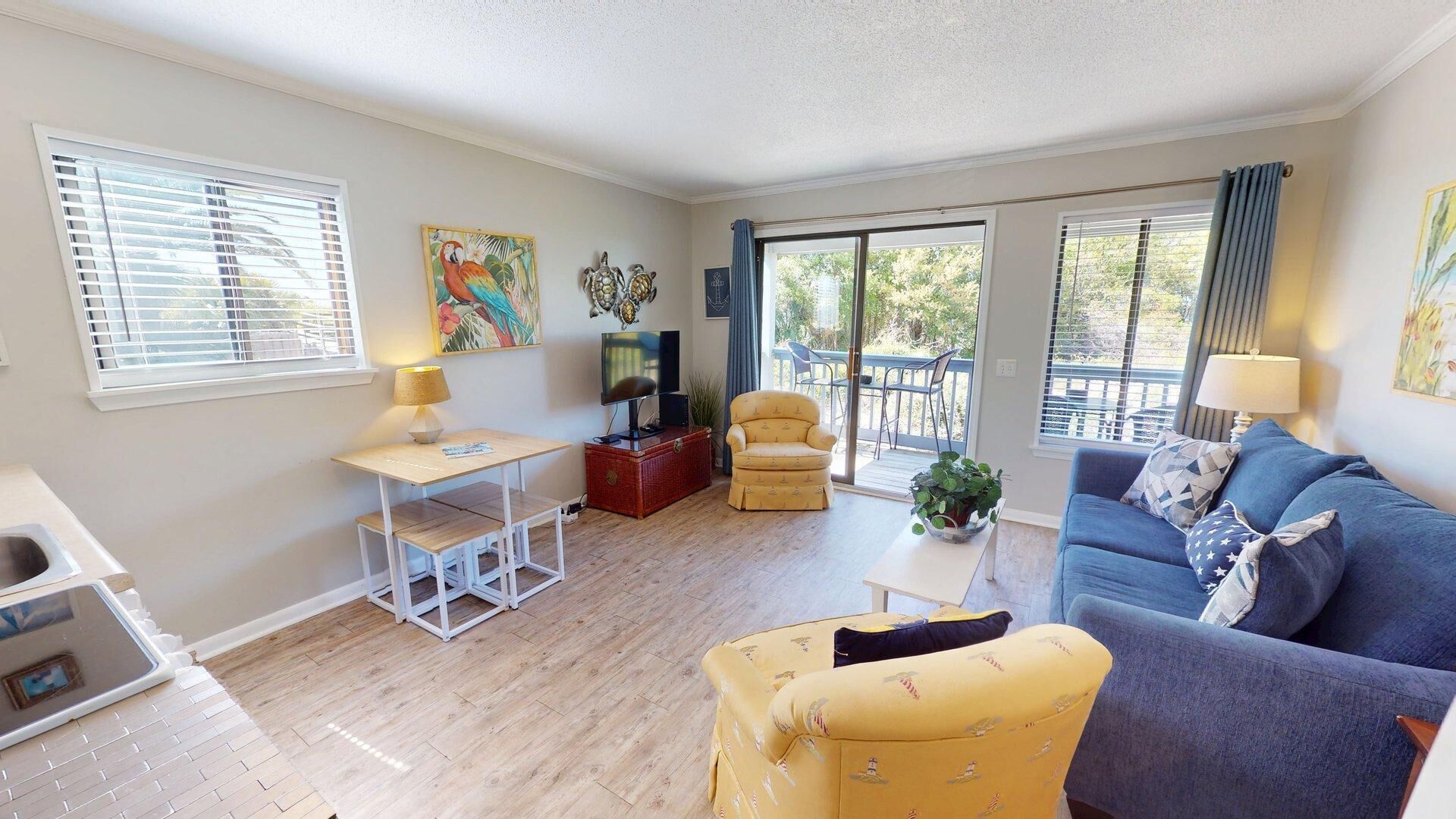 A living room with a sofa, armchair, table, TV, and a balcony with a view.