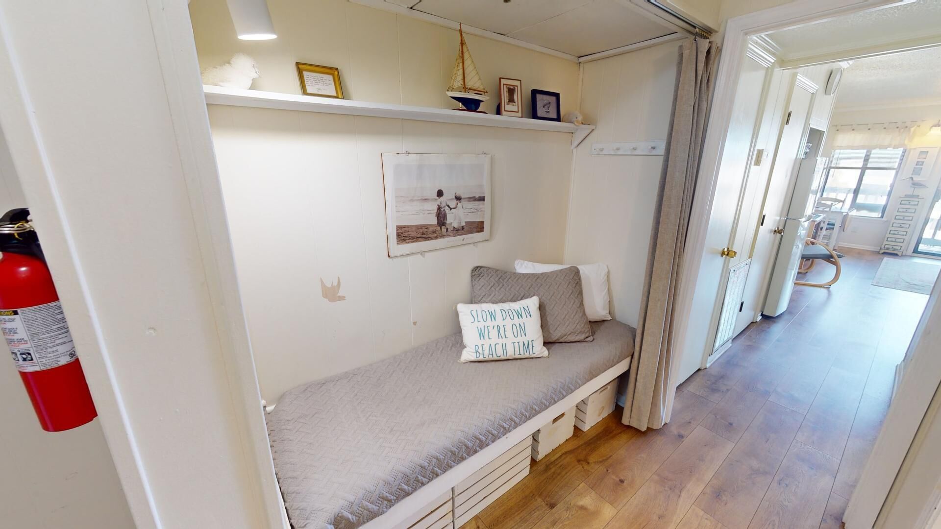 A cozy room with a bed, a shelf with decorative items, a framed picture, and a fire extinguisher.