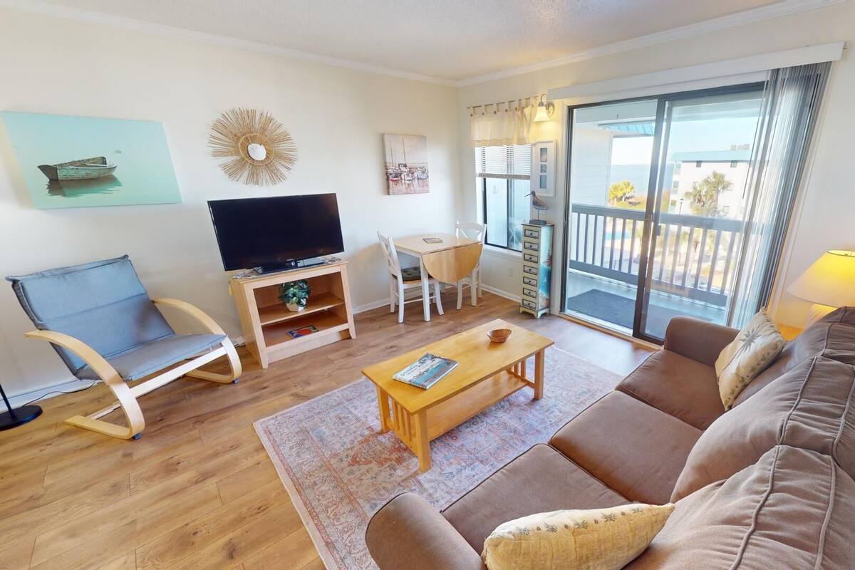 A living room with a sofa, a TV, a dining table, and a balcony with a view.