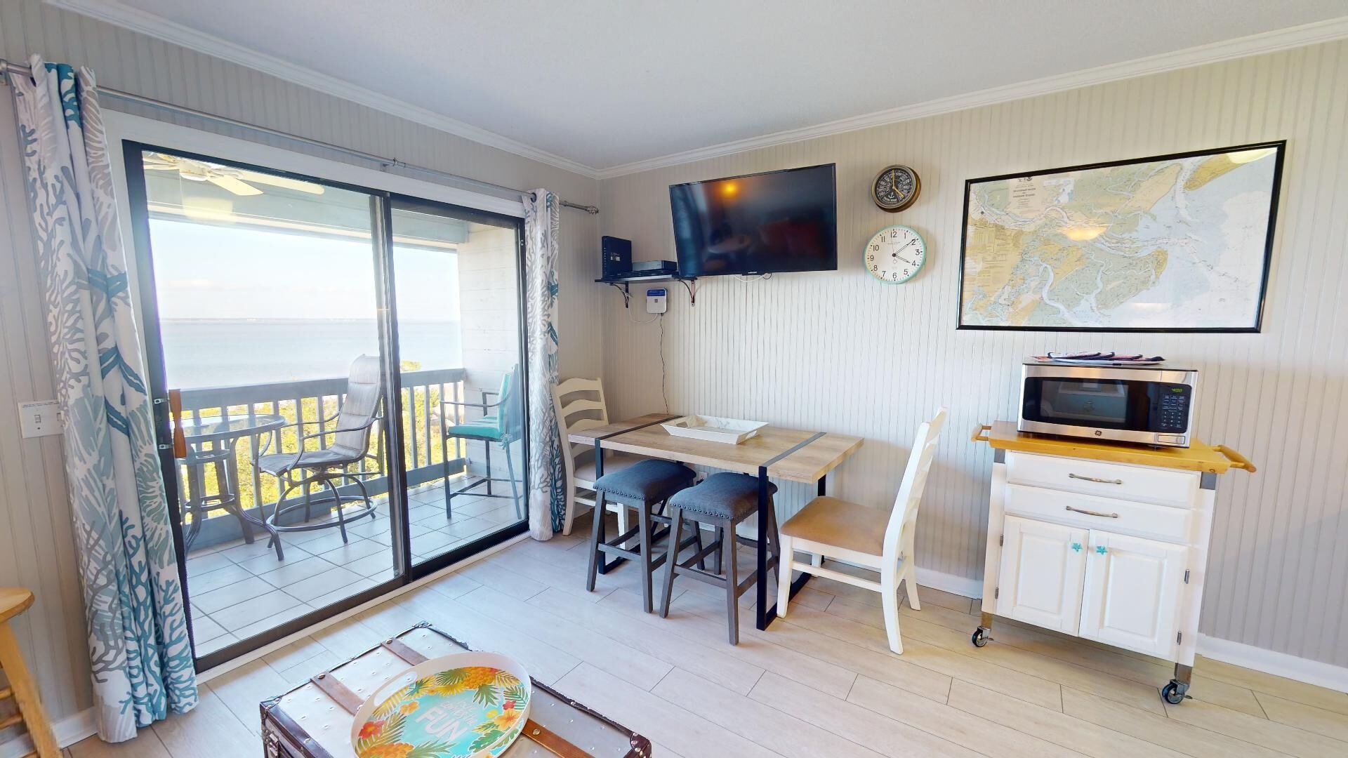 A room with a sliding glass door leading to a balcony, a TV mounted on the wall, a microwave on a cart, and a map on the wall.