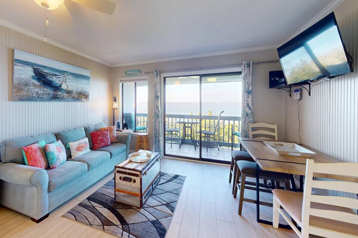 A cozy living room with a sofa, a small table, a TV, and a balcony with a view.
