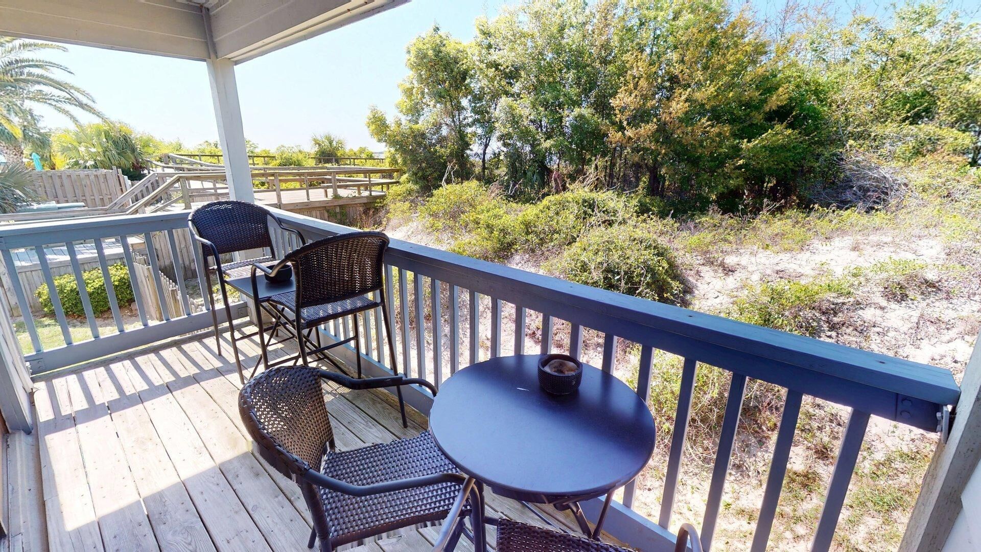 A covered outdoor deck with wooden flooring, metal railings, and wicker furniture.