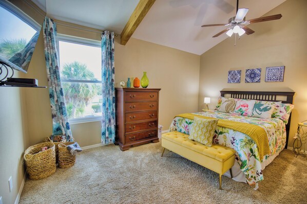 A bedroom with a bed, a dresser, a bench, a ceiling fan, and a window with curtains.