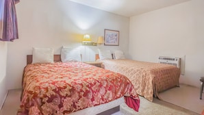 A hotel room with two beds, a nightstand with lamps, a framed picture on the wall, and an air conditioning unit. - Heart of Dixie Motel Near Auburn AL (Dadeville)