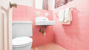 Un baño con azulejos rosas, un inodoro blanco, un lavamanos blanco y una toalla colgada en un perchero.