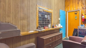 A room with wooden paneling, a blue door, a desk with various items, a brown dresser, and a purple chair. - Heart of Dixie Motel Near Auburn AL (Dadeville)