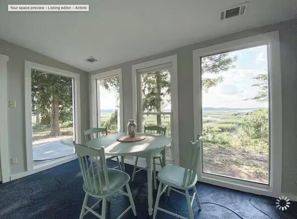 A room with a large window, a table with chairs, and a view of a green landscape.