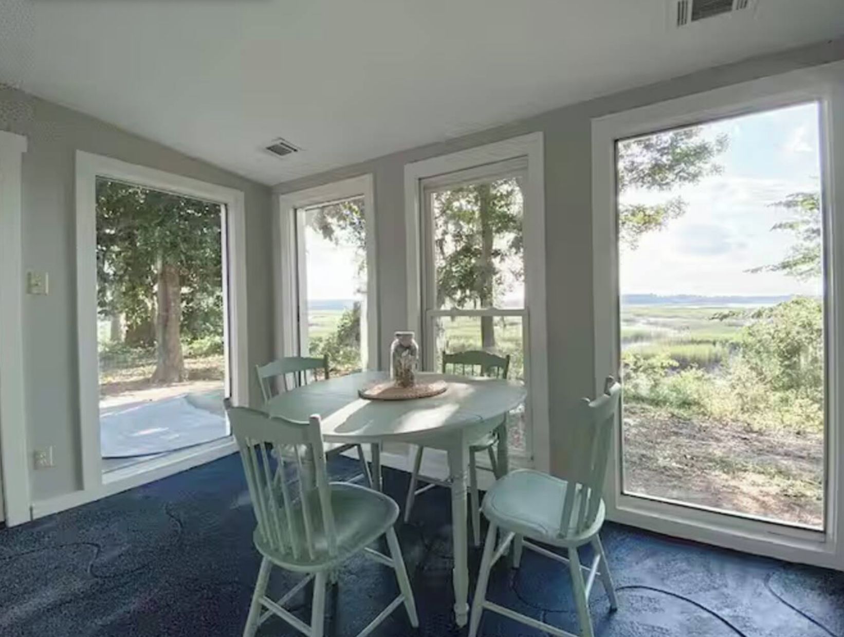 A room with a large window, a table with chairs, and a view of a green landscape.