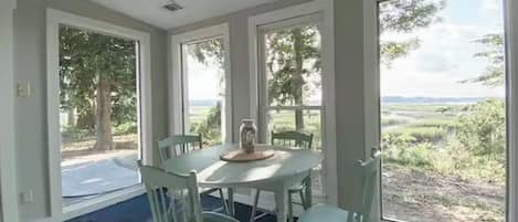 A room with a large window, a table with chairs, and a view of a green landscape.