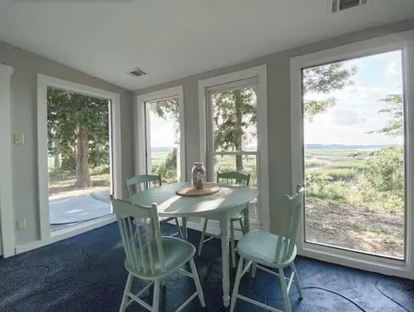 Une pièce dotée d’une grande fenêtre, d’une table avec des chaises et offrant une vue sur un paysage verdoyant.