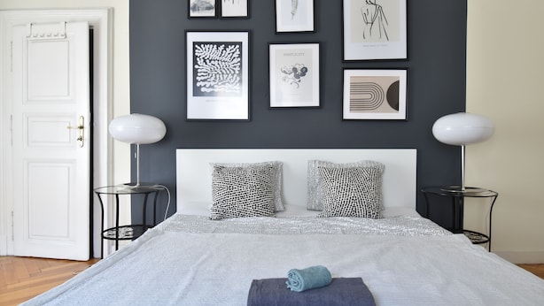 A bedroom with a bed, two bedside tables, a white door, and a wall with framed artwork.