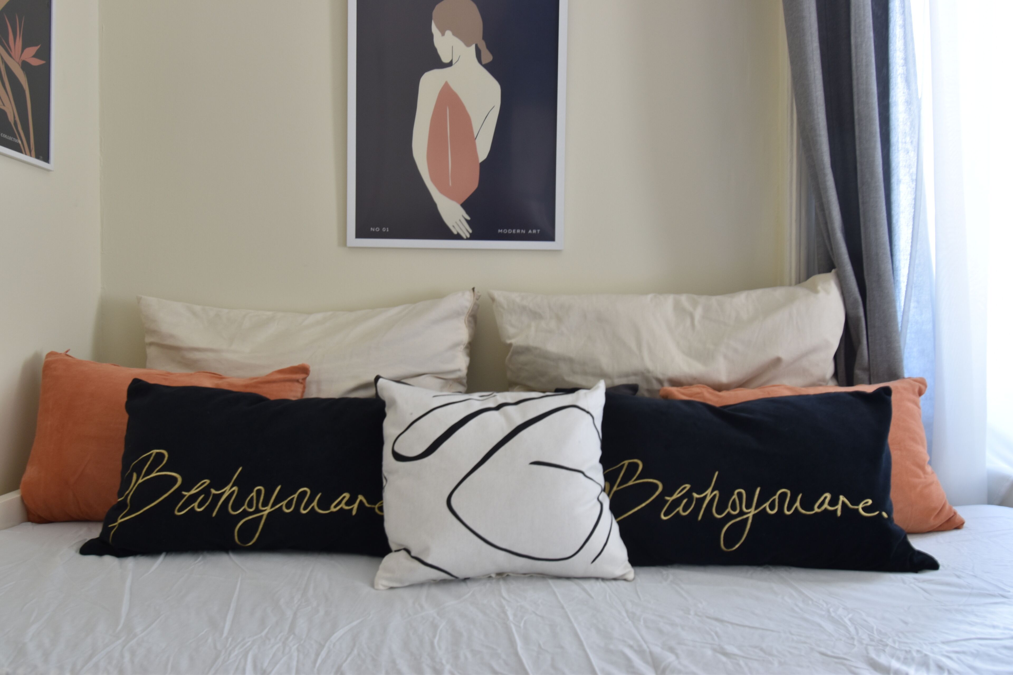 A bed with three pillows, two black and one white, with the word "Bohoyouane" on them.