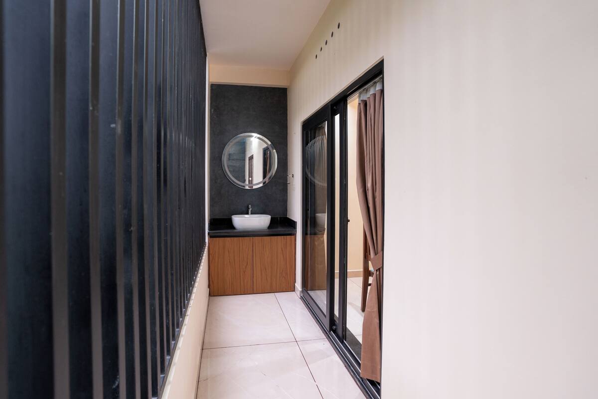 Ein schmaler Flur mit einem modernen Badezimmer, das ein Waschbecken, einen Spiegel und Glastüren umfasst.