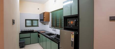 A compact kitchen with green cabinets, a black countertop, a built-in oven, and a microwave.
