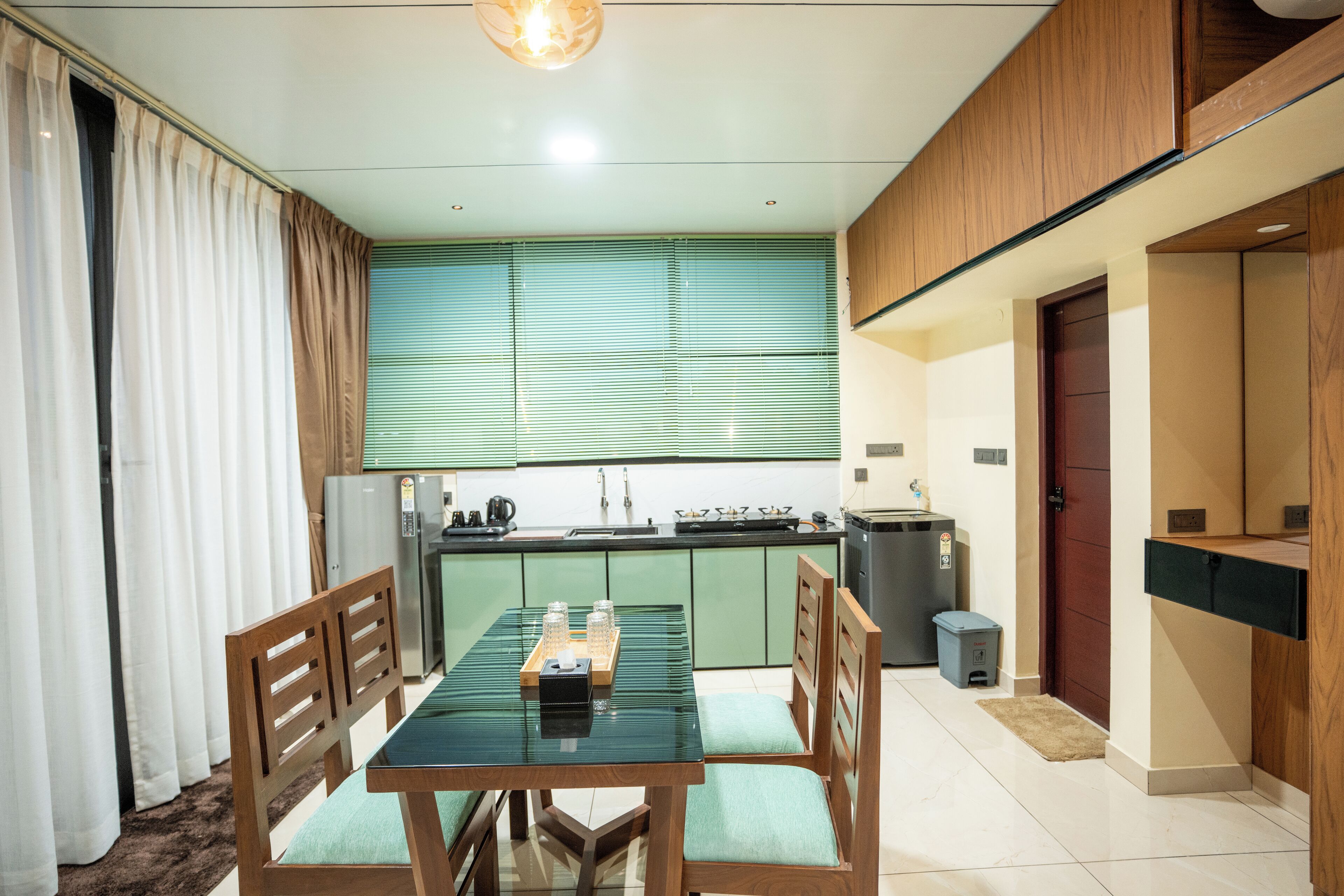 Een moderne keuken met groene kastjes, een eettafel met stoelen en een kleine prullenbak.