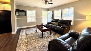A living room with a dark brown leather sofa, a coffee table, and a ceiling fan. - Waterfront Beaufort Home - 3 Miles to Parris Island & Downtown! (Beaufort)