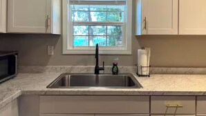 A kitchen with white cabinets, a stainless steel sink, a window with blinds, and a microwave. - Waterfront Beaufort Home - 3 Miles to Parris Island & Downtown! (Beaufort)