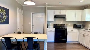 A modern kitchen with white cabinets, a black stove, and a microwave. There is a dining table with chairs. - Waterfront Beaufort Home - 3 Miles to Parris Island & Downtown! (Beaufort)