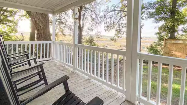 A covered porch with wooden benches and a white railing, overlooking a grassy area with trees. - Waterfront Beaufort Home - 3 Miles to Parris Island & Downtown! (Beaufort)