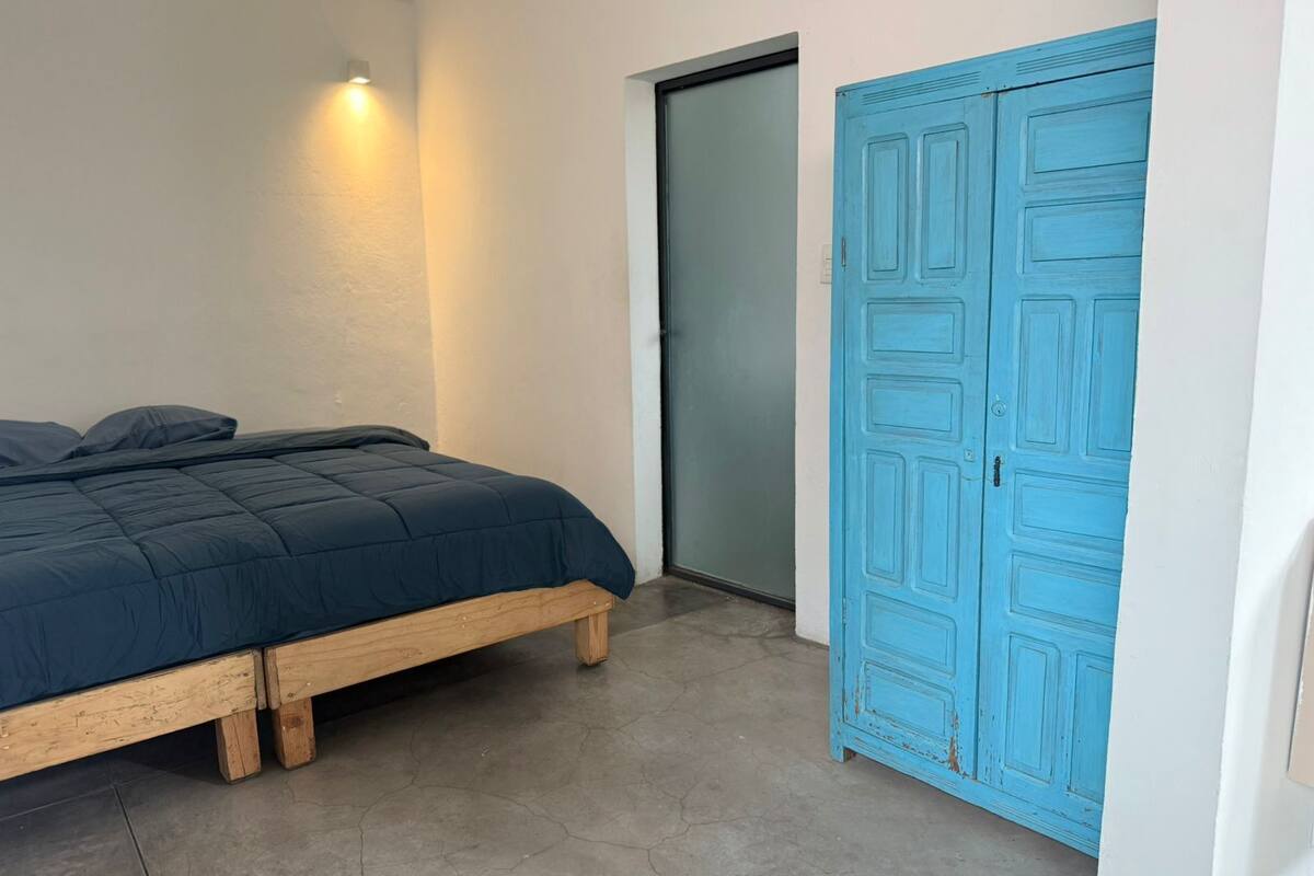 A bedroom with a bed, a blue door, and a light fixture on the wall.