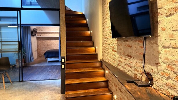 A staircase with wooden steps leading to a room with a TV mounted on a brick wall. - Casa Hoja Azul (San Miguel de Allende)