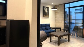 A modern living room with a sofa, a coffee table, and a TV. There is a large window providing a view of the outside. - Casa Hoja Azul (San Miguel de Allende)