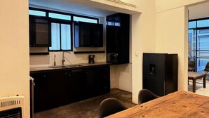 A compact kitchen with dark cabinets, a wooden dining table, and a refrigerator. - Casa Hoja Azul (San Miguel de Allende)