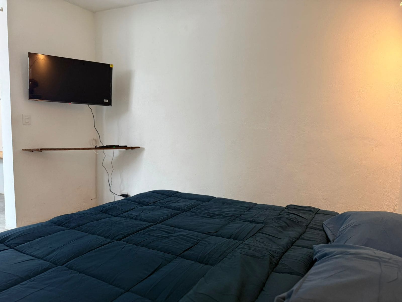 Quarto com cama, televisão fixada na parede e tomada elétrica.