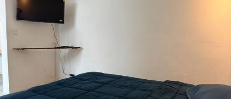 Quarto com cama, televisão fixada na parede e tomada elétrica.