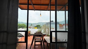 A view from a room with a wooden ceiling and large windows, overlooking a terrace with a table and chairs, and a cityscape in the distance. - Casa Hoja Azul (San Miguel de Allende)