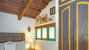 Een slaapkamer met een houten plafond, een groot bed met witte beddengoed, een nachtkastje met een lamp en een garderobe met gele accenten.