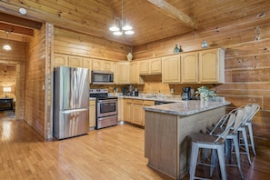 A spacious kitchen with wooden cabinetry, stainless steel appliances, and a central island with bar stools. - River View Dog Friendly Game Room w Hot Tub (Sevierville)