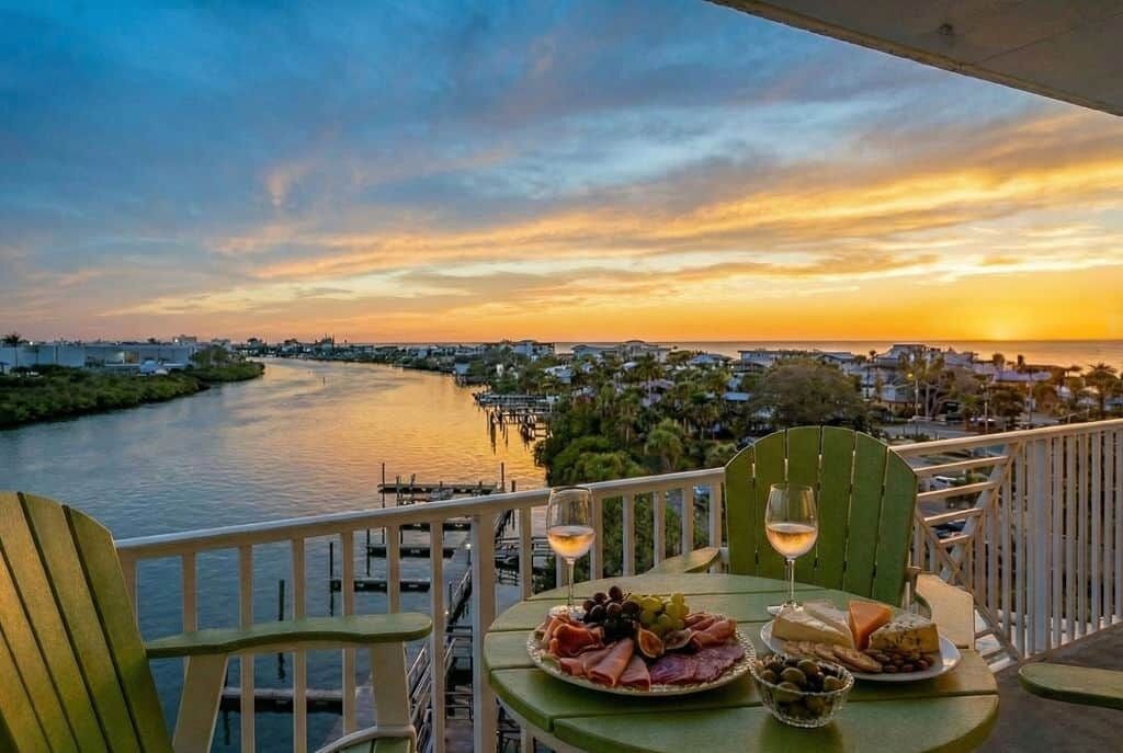 A balcony with a table set for a meal, overlooking a river and cityscape during sunset.