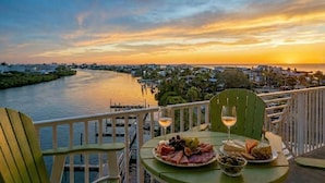 A balcony with a table set for a meal, overlooking a river and cityscape during sunset.